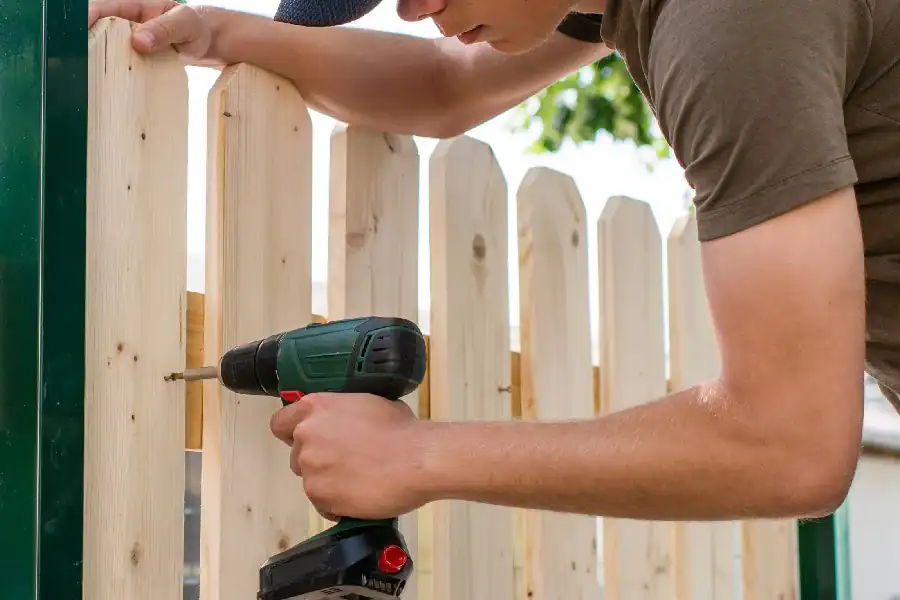 man attaching wood onto wrought iron fence.webp